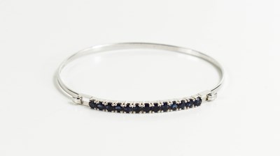 Lot 165 - An 18ct white gold and sapphire bangle, the...